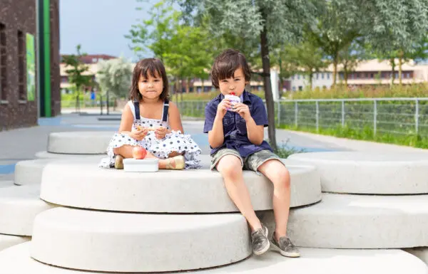 Jongen gebruikt preparaat zittend met zusje op schoolplein.