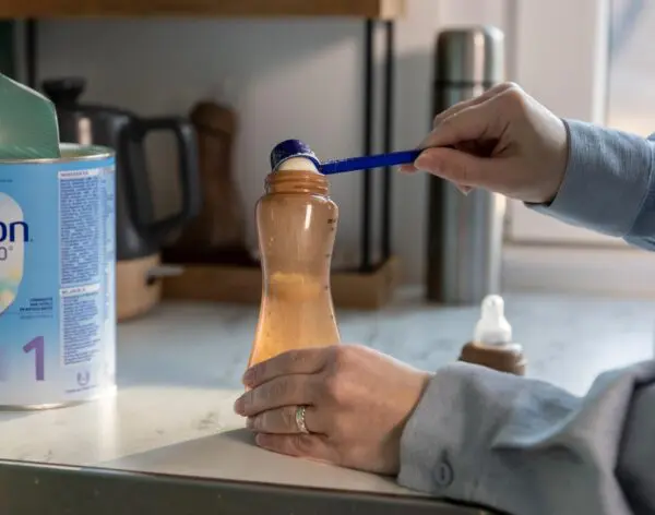 Vrouw doet dieetzuigelingenvoeding met maatschepje in een fles.