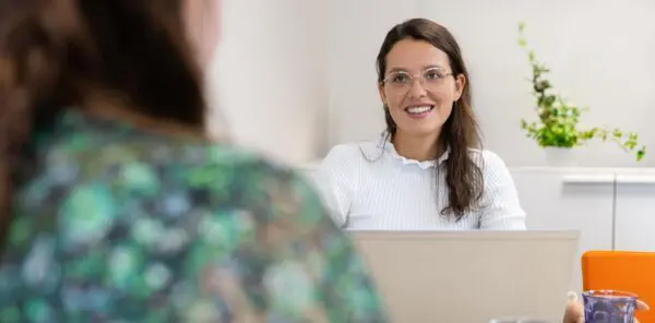 Vrouw heeft een consult met een andere vrouw en zit achter haar laptop.