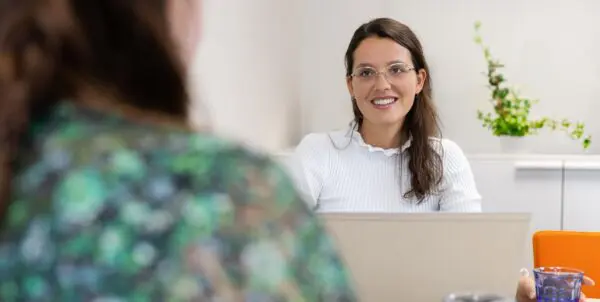 Vrouw in gesprek achter een laptop met een andere vrouw.